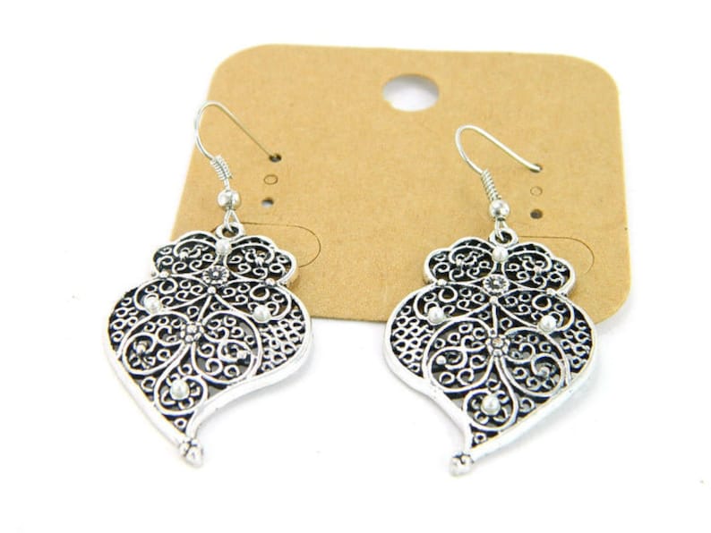 May include: A pair of silver filigree earrings with a heart shape and small clear rhinestones.