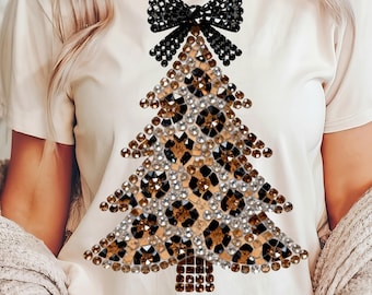 May include: A cream-colored t-shirt featuring a Christmas tree design. The tree is made of leopard print and embellished with rhinestones. A black rhinestone bow sits atop the tree. The shirt has short sleeves.