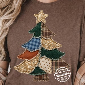 May include: A brown t-shirt featuring a graphic of a Christmas tree constructed from various fabric patches including corduroy, plaid, and floral patterns. The tree is topped with a star and includes a circular stamp with the text ORIGINAL.