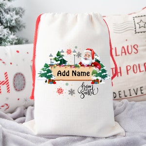 May include: A white drawstring gift bag with a festive Santa Claus design. The design includes a wooden sign that says "Add Name" and the words "from Santa". The bag has red drawstrings and is perfect for Christmas.