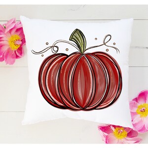 May include: A white pillow with a red and black hand-drawn pumpkin design. The pumpkin has a green stem and a brown vine with gold dots.