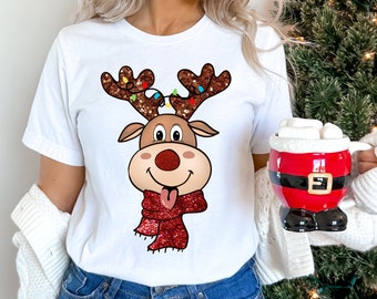 May include: White t-shirt with a cartoon reindeer wearing a red glitter scarf and a string of Christmas lights on its antlers.