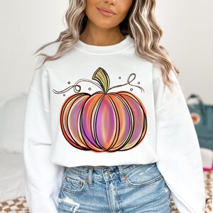 May include: White sweatshirt with a colorful, hand-drawn pumpkin design. The pumpkin has orange, pink, and purple stripes and a green stem.