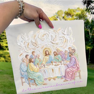May include: A cream-colored artwork depicting the Last Supper, with Jesus at the center, surrounded by disciples. Above, white doves are sculpted. The phrase "do this in remembrance of me" is written in a cursive font.