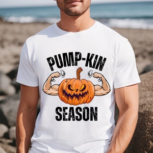 May include: White t-shirt with a graphic of a jack-o'-lantern lifting weights. The text "Pump-Kin Season" is printed below the image.