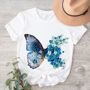 May include: White t-shirt with a blue butterfly and blue flowers printed on the front.