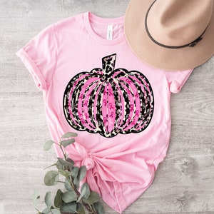 May include: Pink t-shirt with a pink and black pumpkin design. The pumpkin is made up of pink ribbons and has a leopard print pattern.