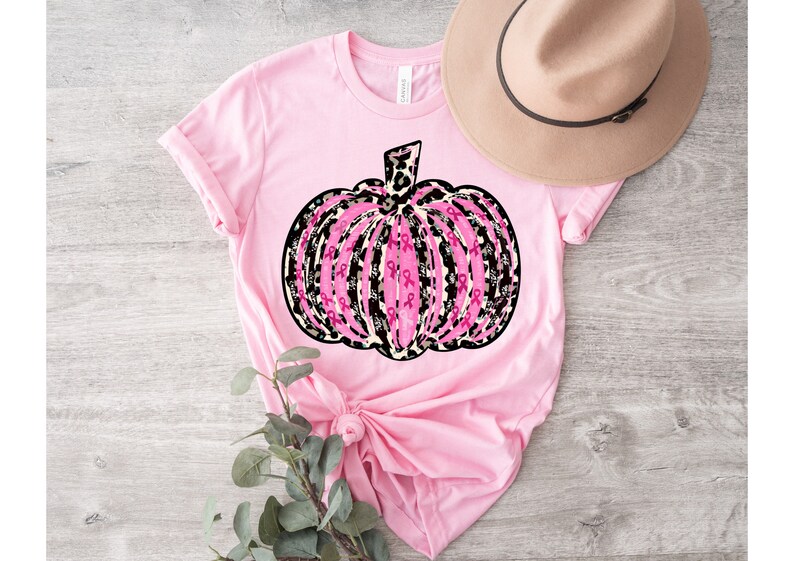 May include: Pink t-shirt with a pink and black pumpkin design. The pumpkin is made up of pink ribbons and has a leopard print pattern.
