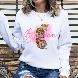 Pu&ograve; includere: Felpa bianca con un design acquerellato rosa che presenta un leopardo con accenti dorati e la parola "Boss" scritta in rosa.