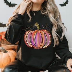 May include: Black sweatshirt with a colorful pumpkin graphic. The pumpkin is outlined in black and has a gradient of orange, pink, and purple.