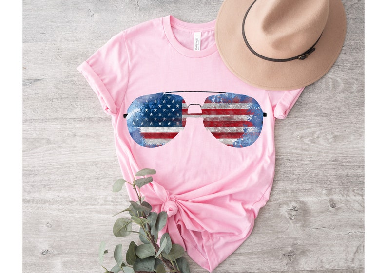 K&ouml;nnte beinhalten: Pinkes T-Shirt mit einem Aufdruck von Aviator-Sonnenbrillen mit amerikanischem Flaggenmuster.