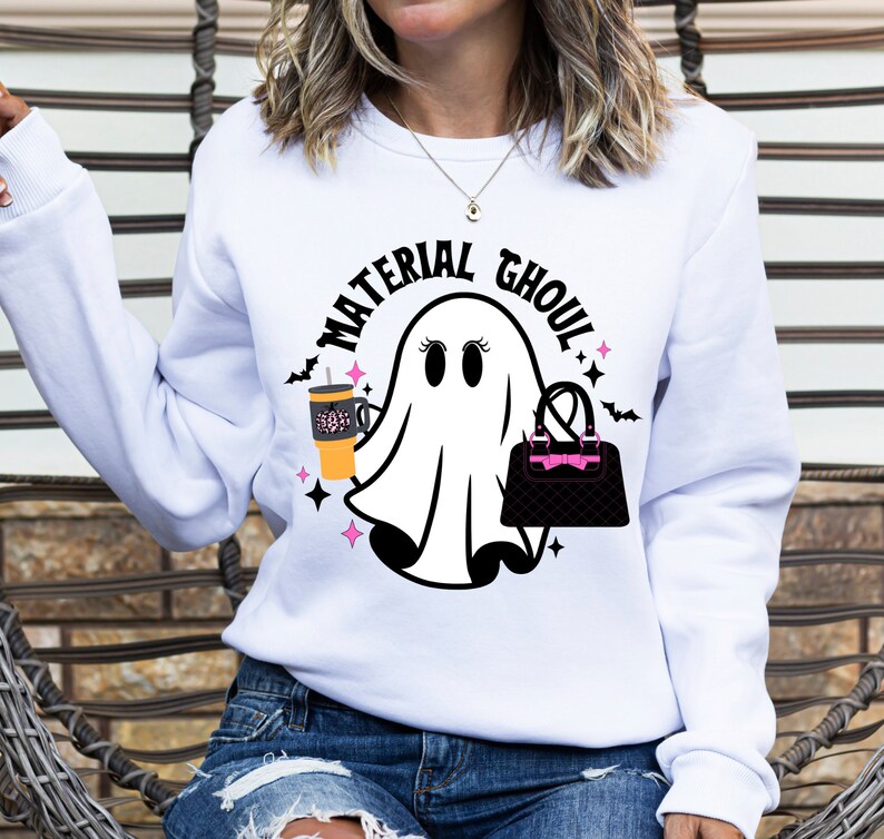 May include: White sweatshirt with a ghost graphic holding a coffee cup and a purse. The text "Material Ghoul" is written in a black circle around the ghost.