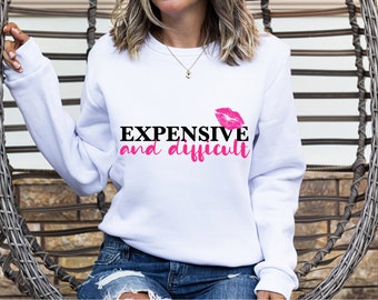 Könnte beinhalten: Weißer Pullover mit schwarzem Text, der "EXPENSIVE and difficult" lautet, mit einem rosafarbenen Lippenstift-Druck über dem Text.