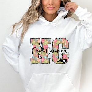 May include: White hooded sweatshirt with a floral design of the letters "NC" and the text "North Carolina" with a small outline of the state of North Carolina.