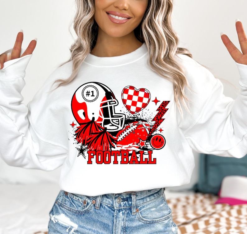 May include: White sweatshirt with a red, black, and white graphic design featuring a football helmet, a heart, a lightning bolt, and the word "FOOTBALL".