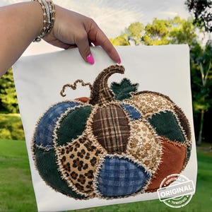 Puede incluir: Una calabaza decorativa de tela con un diseño de patchwork que presenta varias texturas y patrones, incluyendo cuadros azules, pana verde oscuro, cuadros marrones, estampado de leopardo y tela floral beige, con bordes deshilachados.