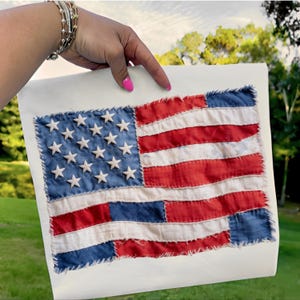 Könnte beinhalten: Eine handgefertigte amerikanische Flagge mit roten und weißen Streifen und einem blauen Feld mit weißen Sternen. Die Flagge besteht aus Stoff und hat ein Vintage-Patchwork-Aussehen. Die Flagge wird auf weißem Hintergrund präsentiert.