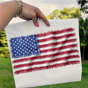 May include: A white rectangular flag featuring a distressed American flag design. The flag has a blue square with white stars in the upper left corner and red and white stripes. The edges of the flag have a frayed, distressed look.