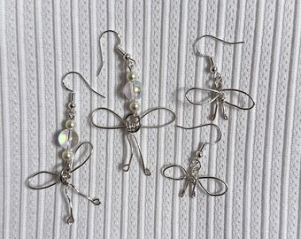 May include: Four pairs of silver earrings with iridescent white beads and wire bows. The earrings are delicate and feminine.