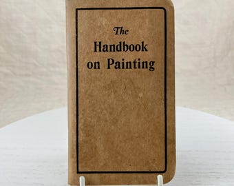 Op de afbeelding: Een bruin, ingebonden boek met de titel "The Handbook on Painting" gedrukt in zwart.