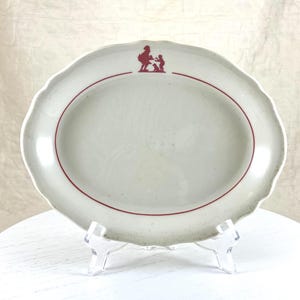May include: A white oval serving dish with a red rim and a red silhouette of a woman and child on the front.