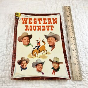 Puede incluir: Una portada de cómic vintage de Dell con el título "Western Roundup" en un esquema de colores rojo y blanco. La portada presenta cinco vaqueros, incluido uno montando a caballo, y un fondo de ladrillos.