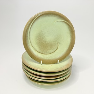May include: A stack of six round ceramic plates featuring a light mint green center and a contrasting tan brown rim. Each plate has a subtle, embossed spiral design that curves across the surface, creating a textured look on the glazed finish.