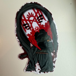 May include: A sticker featuring a stylized illustration of a figure in a dark cloak and mask. The mask is white with red markings and a red, blood-like design. The figure is in a dark green outfit.