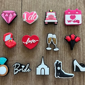 May include: A collection of colorful wedding-themed charms. Includes a pink diamond, a heart with "I do" text, a pink car, a calendar, a ring box, a heart with "love" text, champagne glasses, red tulips, a ring, the word "Bride", a church, a bride and groom, and a high heel shoe.