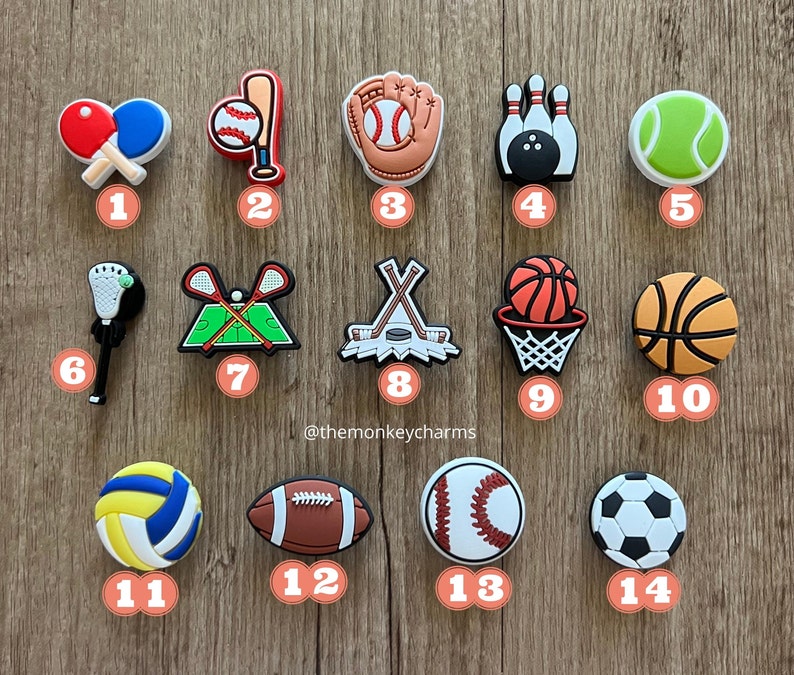 K&ouml;nnte beinhalten: Eine Sammlung von Sport-Themen-Anh&auml;ngern, darunter Tischtennisschl&auml;ger, ein Baseball und Schl&auml;ger, ein Baseballhandschuh, Bowlingkegel, ein Tennisball, ein Lacrosseschl&auml;ger, eine Feldhockeyszene, Hockeyschl&auml;ger und ein Puck, ein Basketball in einem Korb, ein Basketball, ein Volleyball, ein Football, ein Baseball und ein Fu&szlig;ball.