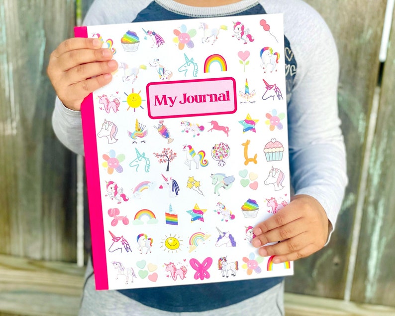 May include: A white journal with a pink border. The front cover is decorated with colorful unicorn stickers and the words 'My Journal' in a pink rectangle.