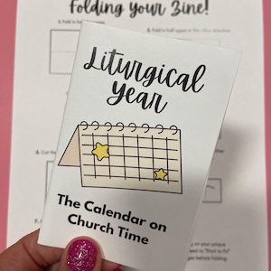 Peut inclure: Un livret blanc intitulé "Liturgical Year" avec une illustration de calendrier et le texte "The Calendar on Church Time". Le livret est tenu sur un fond rose avec des instructions pour plier un fanzine.