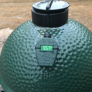 Puede incluir: Ahumador de cerámica verde en forma de huevo con una tapa negra y un termómetro digital que marca 55,7 grados Fahrenheit.