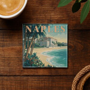 May include: Square glass coaster featuring a vintage illustration of Naples, Italy. The artwork depicts a beach scene with palm trees, a grand building, and the word "NAPLES" in a serif font. The coaster has a glossy finish and is set on a wooden surface.