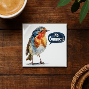 May include: Square coaster featuring a watercolor painting of a European robin with blue, orange, and brown feathers. A speech bubble says "No Comment". The coaster is on a wooden surface.