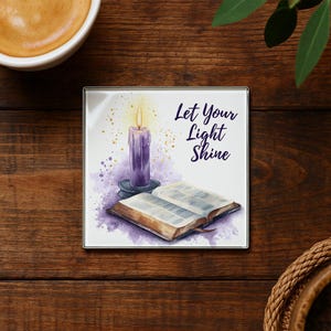 May include: Square coaster with a watercolor design featuring a purple candle, an open book, and the text "Let Your Light Shine." The coaster has a silver border and is set on a wooden surface.