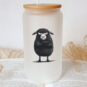 May include: A frosted glass water bottle with a bamboo lid and a black and white illustration of a sheep with a grumpy expression. The sheep is standing with its arms crossed.