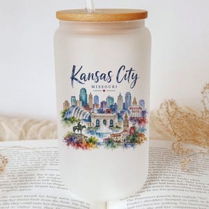 A white glass jar with a straw, featuring a colorful illustration of the skyline of Kansas City, Missouri.