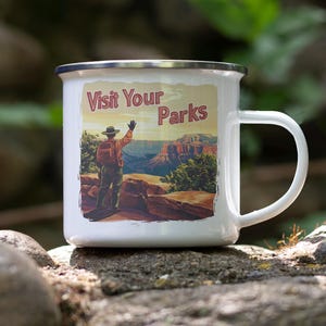 May include: White enamel mug with a silver rim featuring a vintage-style illustration. The image depicts a person in a hat and backpack overlooking a canyon, with the text "Visit Your Parks". A perfect gift for outdoor enthusiasts.