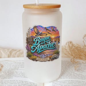 May include: A frosted glass tumbler with a bamboo lid and a clear straw. The front features a colorful graphic of the Bosque del Apache National Wildlife Refuge, depicting birds in flight over a sunset landscape with desert flora and text.