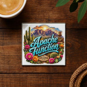 May include: A square coaster featuring a colorful illustration of the Arizona desert with saguaro cacti, blooming flowers, and mountains under a sunrise. The text reads Apache Junction and Arizona Est. 1872 in a bold, blue, stylized script font.