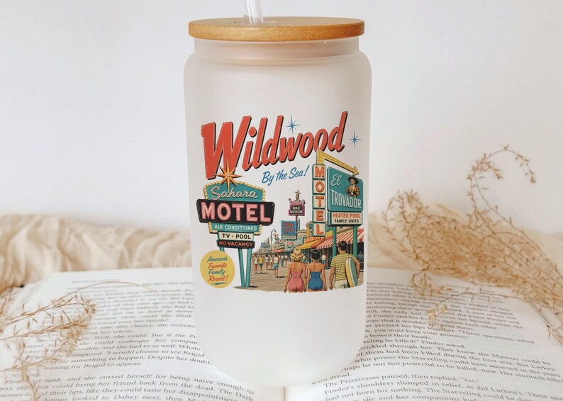 A clear glass tumbler with a straw, featuring a vintage motel sign and a vintage motel sign, placed on top of an open book.