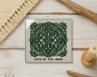 May include: Square glass coaster with a green Celtic knot design and the text "LUCK OF THE IRISH". The coaster has a light gray background and a silver border. The coaster is on a light wood surface.