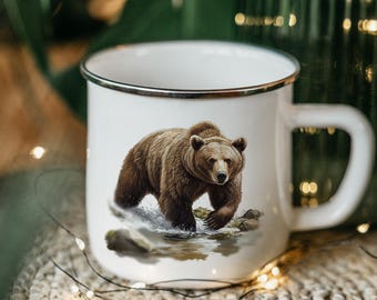 May include: White enamel mug with a brown bear illustration. The bear is standing in a stream with rocks and water. The mug has a silver rim.