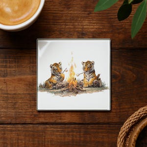 May include: Square coaster featuring two tiger cubs roasting marshmallows over a campfire. The cubs are depicted in a detailed watercolor style, with orange and black stripes. The coaster has a white background and a silver edge.