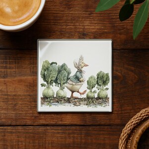 May include: Square coaster with a whimsical illustration of a duck wearing a bonnet and jacket, walking past a row of green cabbages. The duck is depicted in soft watercolor tones, set against a white background.