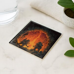 May include: Square coaster featuring a fantasy scene of two figures in silhouette, facing a fiery portal. The artwork is set against a dark background with orange and yellow hues. The coaster is on a white surface, with a glass and a plant nearby.