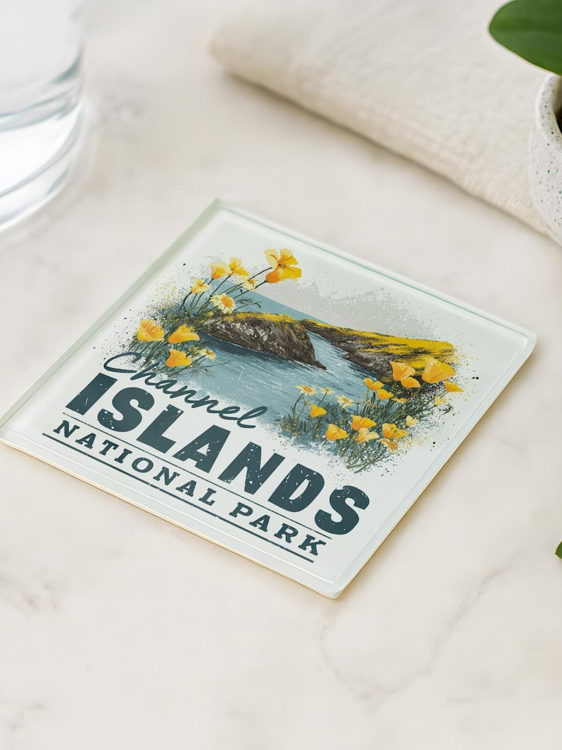 a coaster with a scenic illustration of the Channel Islands National Park, accompanied by a glass of water and a potted plant on a marble surface.