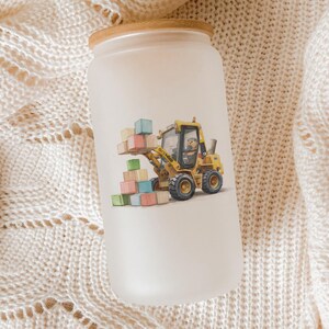 May include: Frosted glass tumbler with a bamboo lid. The tumbler features a colorful illustration of a yellow construction vehicle carrying building blocks. The design is playful and suitable for children.
