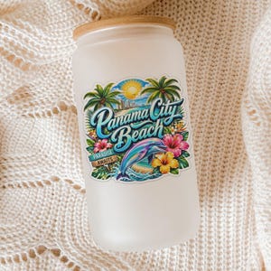 May include: A frosted glass tumbler with a bamboo lid featuring a colorful graphic of Panama City Beach, palm trees, a sun, hibiscus flowers, and a dolphin, with the text Panama City Beach and Paradise Awaits printed on the front surface.